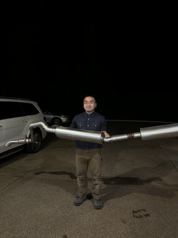 Danny, the founder, holding an exhaust component next to his NC2 Miata at night